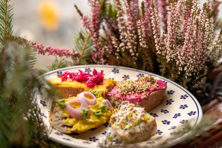 ein geblümter Teller mit vier Broten mit bunten Gemüseaufstrichen